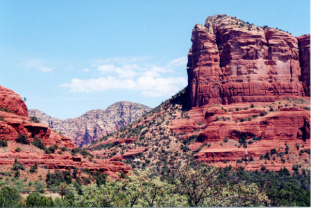 [Rocks and cliffs of different heights pepper the image. The ones in the distance are more of a tan color than red. All rocks have dark green dots of vegetation on them.]